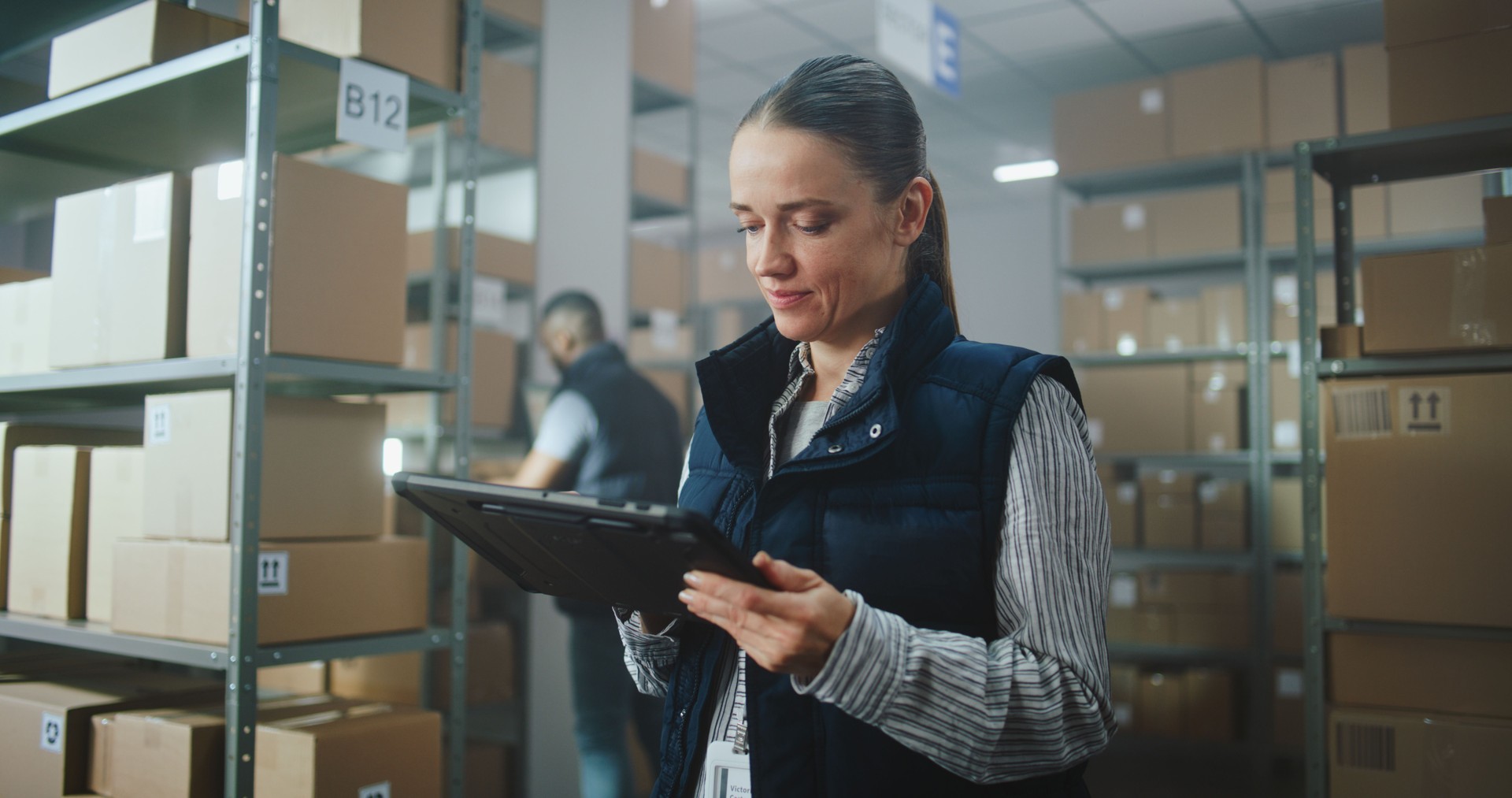 Female Inventory Manager in Warehouse Facility: Uses Tablet Computer, Looks at Camera